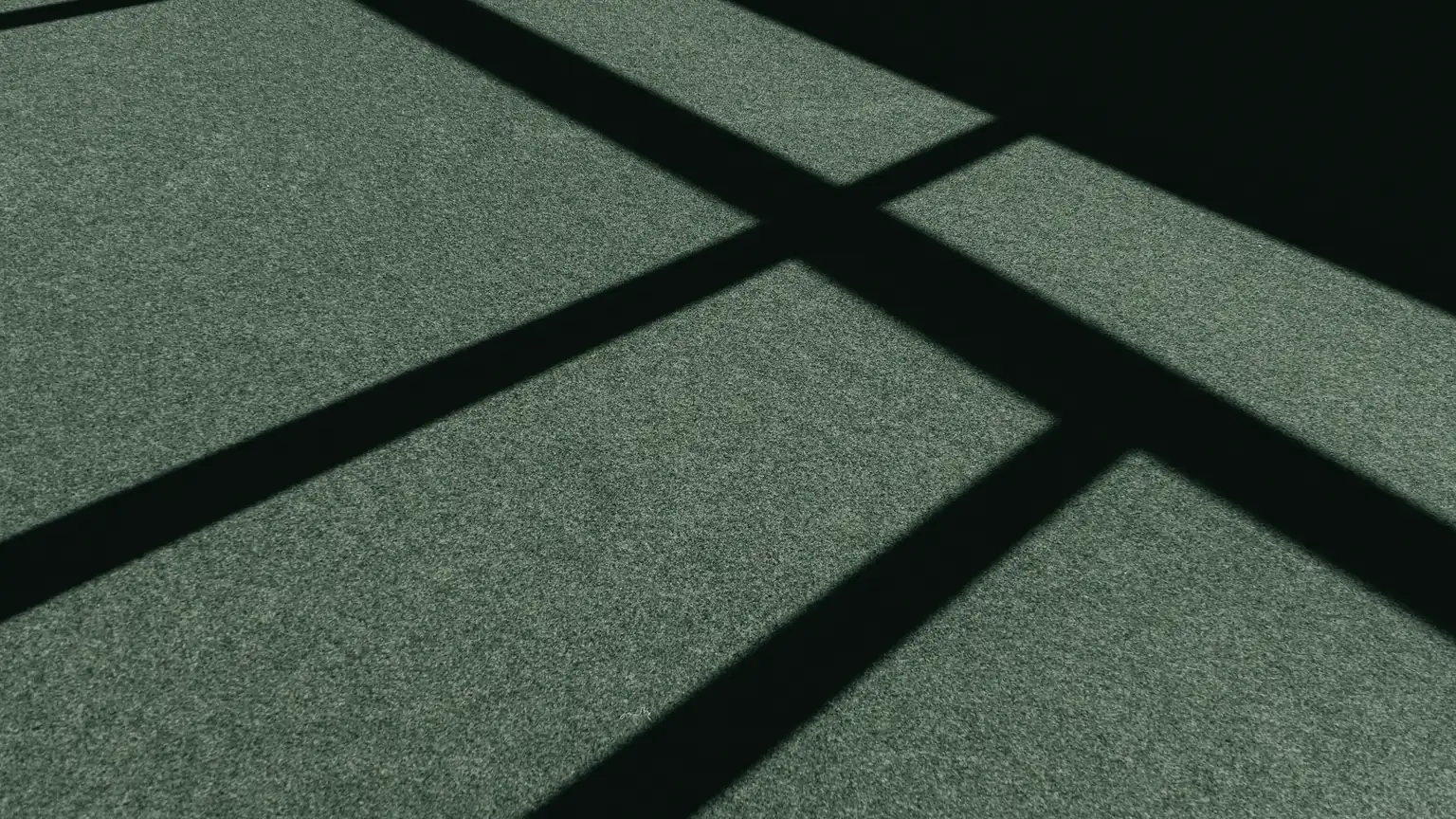 The shadows of a net and its posts fall across a green court.