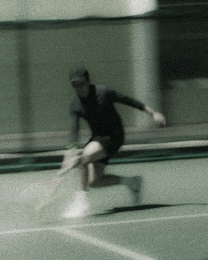 A player runs into a low forehand on a green court, blurred with speed.