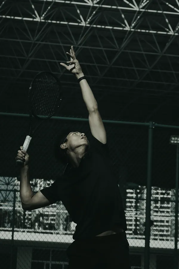 A player in black reaches up to serve under a steel roof.