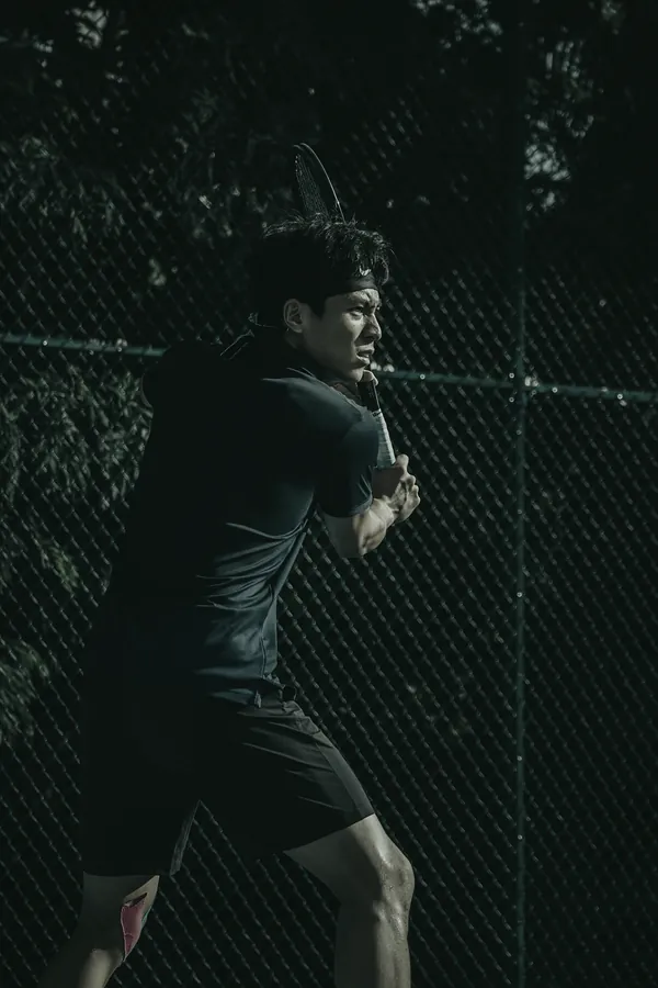 A player in a dark shirt sets up a backhand in front of a green fence.